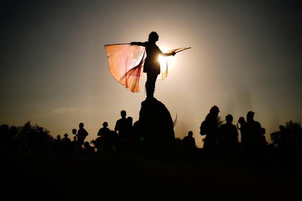 A festival attendee is silhouetted as they stand on top of the stone circle at Worthy Farm. PA