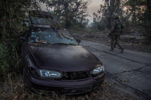 Ukrainian service members walk past a damaged car in Severodonetsk. Reuters