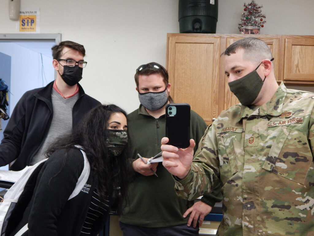 Master Sgt. Joseph Dufault, superintendent, Aircrew Flight Equipment, 375th Operations Support Squadron shows a video on his phone of the August 12, 2020, flooding of the AFE office to graduate students (left to right) Kyle Collier, Astha Bhatnagar, and Cam Loyet. The students are helping Scott's Elevate innovation team to find potential solutions to prevent future flooding. (Photo: Courtesy of Christine Spargur)